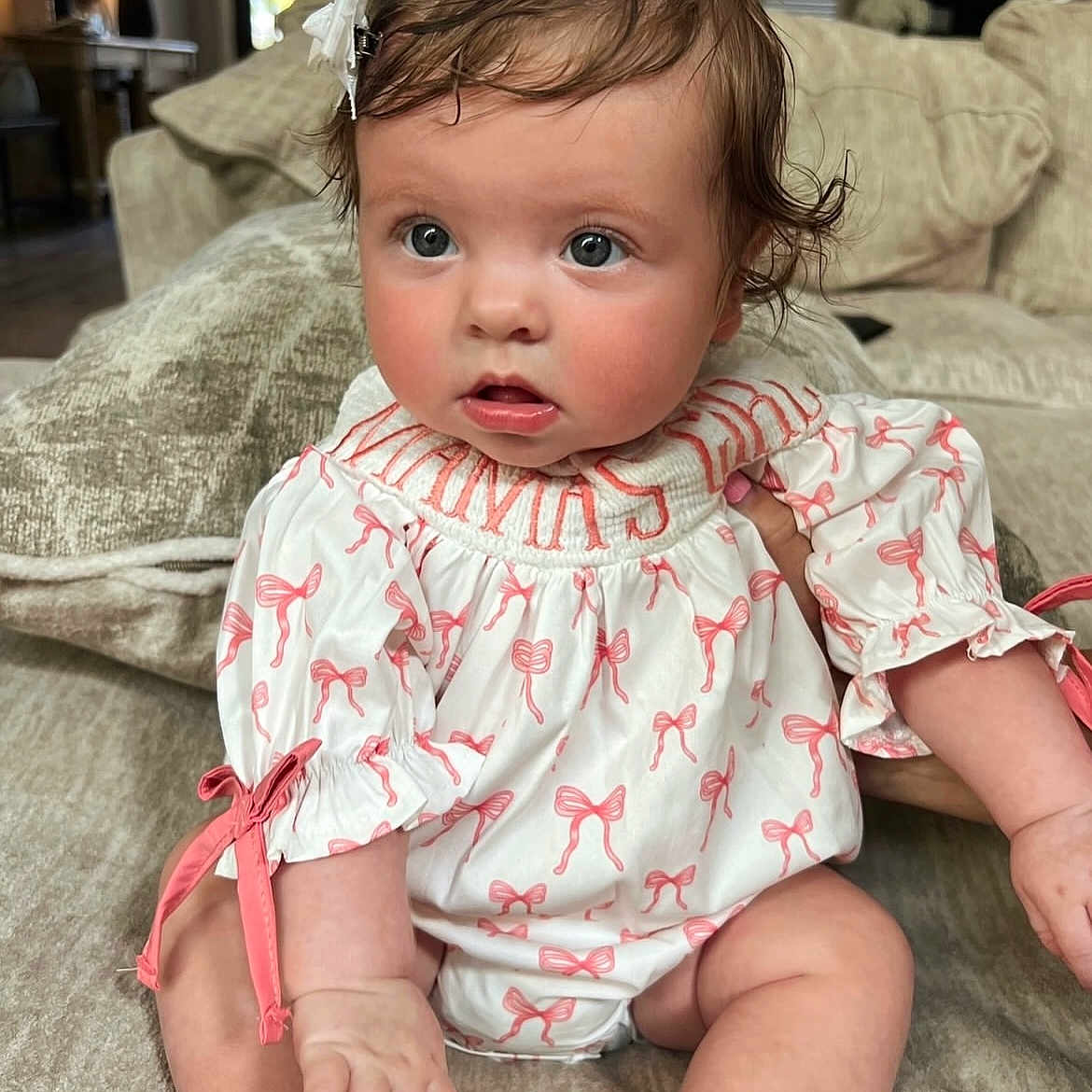 Bella Reece is registered to the contest to win money with this photo: baby, bow, child, comfortable, couch, curly_hair, cute, expression, face, hand, home, indoor, infant, living_room, pink_bows, portrait, sitting, skin, soft_lighting, white_outfit