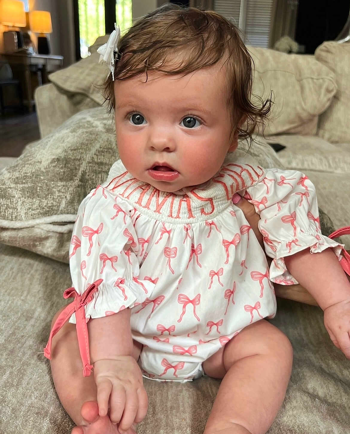 Bella Reece is registered to the contest to win money with this photo: baby, infant, child, curly_hair, bow, white_outfit, pink_bows, couch, living_room, soft_lighting, sitting, cute, portrait, indoor, hand, face, expression, skin, comfortable, home