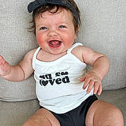 Bella Reece joined the competition — help win amazing prizes! baby, smiling, happy, child, infant, tank_top, headband, bow, sitting, couch, rosy_cheeks, cute, chubby_arms, black_clothing, white_clothing, portrait, indoor, person, young_child, joyful