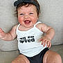 baby, smiling, happy, child, infant, tank_top, headband, bow, sitting, couch, rosy_cheeks, cute, chubby_arms, black_clothing, white_clothing, portrait, indoor, person, young_child, joyful