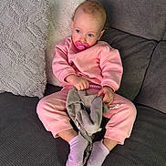 Andréa a rejoint le concours — aidez-le/la à gagner de superbes lots ! child, baby, toddler, pacifier, pink_clothing, socks, couch, pillow, cushion, blanket, soft_toy, earrings, blue_eyes, seated, indoor, cozy, neutral_expression, home_interior, plush_texture, relaxed_pose