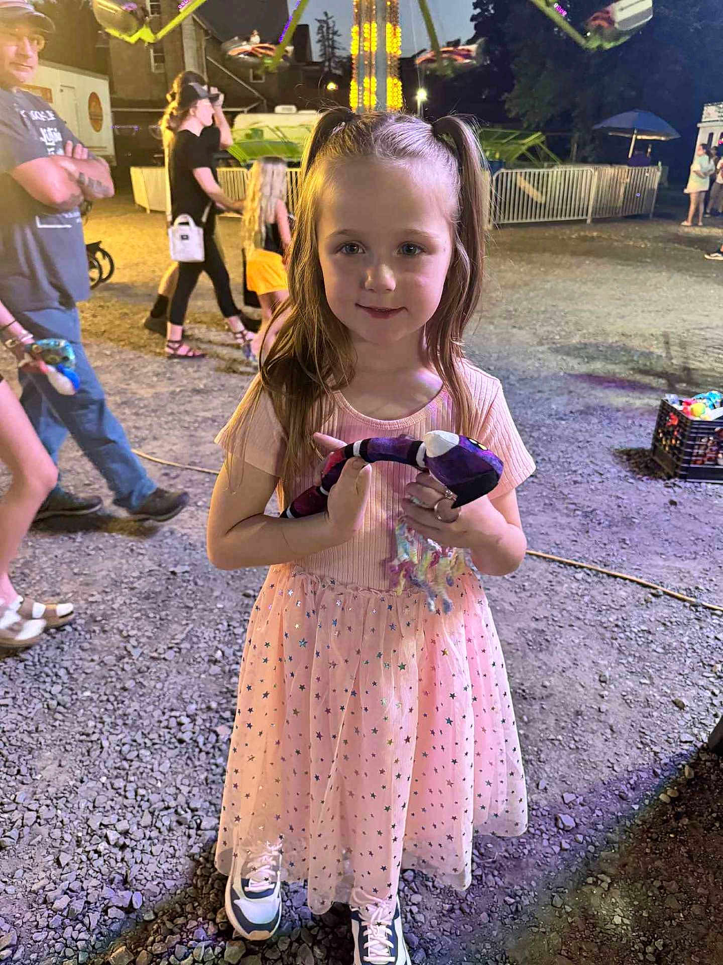 Ava joined the competition — help win amazing prizes! child, girl, pink_dress, stuffed_toy, night, fair, amusement_park, people, gravel, lights, carnival, smiling, outdoor, fun, casual_clothing, sneakers, long_hair, ponytails, family, event