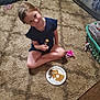 breakfast, carpet, child, clothing, couch, cute, floor, food, fork, hair, home, indoor, laundry_basket, living_room, paper_plate, person, plate, sitting, smile, toy