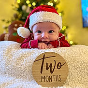 Landon is registered to the contest to win money with this photo: baby, infant, christmas, holiday, santa_hat, red_clothing, blanket, wooden_sign, two_months, decorations, gingerbread_man, christmas_tree, indoors, portrait, cute, smiling, festive, holiday_decor, child, person
