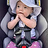 baby, infant, child, car_seat, sunhat, floppy_hat, harness, portrait, sitting, wide_eyed, facial_expression, hands, floral_clothing, purple_pants, vehicle, interior, safety_buckle, close_up, photography, adorable
