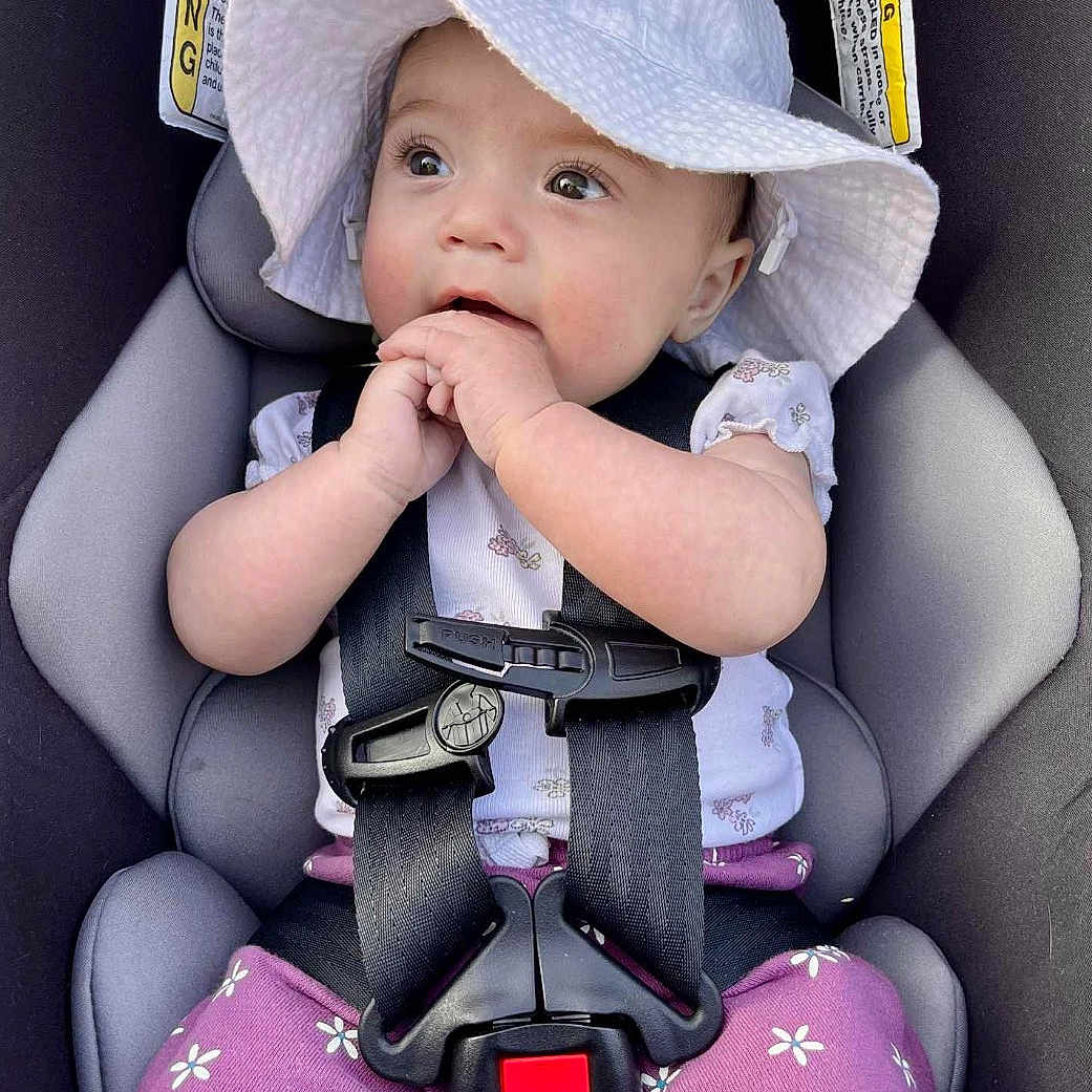 Olivia joined the competition — help win amazing prizes! baby, infant, child, car_seat, sunhat, floppy_hat, harness, portrait, sitting, wide_eyed, facial_expression, hands, floral_clothing, purple_pants, vehicle, interior, safety_buckle, close_up, photography, adorable