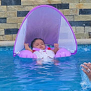 Lylah is registered to the contest to win money with this photo: baby, pool, water, float, purple, sunshade, infant, child, swimming, relaxing, splash, hand, brick_wall, outdoor, summer, leisure, life_jacket, safe, floating, recreation