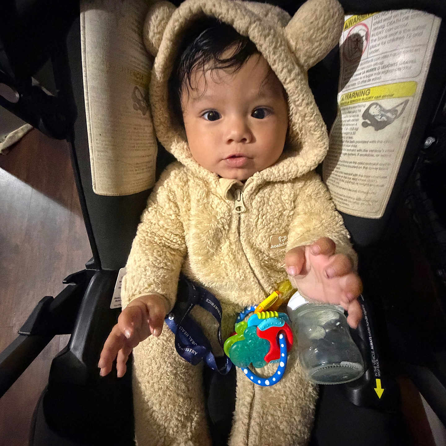 Xander joined the competition — help win amazing prizes! baby, child, car_seat, onesie, fuzzy_clothing, toy, bottle, indoor, cute, expression, infant, curious, seatbelt, portrait, young_child, face, hand, dark_background, cozy, hood