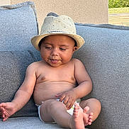 Izac participe au concours pour gagner de l'argent avec cette photo : baby, child, hat, straw_hat, diaper, couch, sofa, gray_couch, outdoor, summer, cute, chubby, skin, bare_chest, foot, sitting, curious, tongue_out, relaxed, natural_light