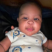 Tyrese joined the competition — help win amazing prizes! baby, infant, child, face, smiling, portrait, close_up, indoors, onesie, clothing, lion_pattern, dark_background, seated, looking_at_camera, happy, cute, person, head, arms, photography