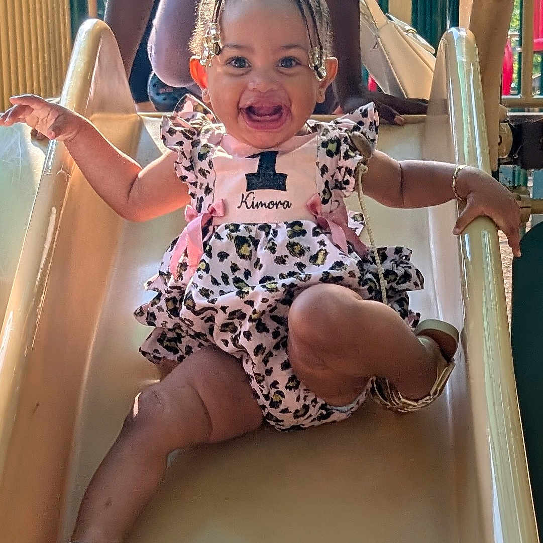 Kimora joined the competition — help win amazing prizes! activity, baby, bow, braids, child, cute, dress, fun, happy, joy, leisure, outdoor, park, person, playground, ramp, sandals, slide, smiling, summer