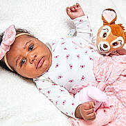 Hope Aÿla a rejoint le concours — aidez-le/la à gagner de superbes lots ! baby, infant, headband, bow, plush_toy, stuffed_animal, blanket, pink_dress, floral_pattern, lying_down, portrait, chubby_cheeks, big_eyes, hand, skin, curly_hair, soft_texture, cozy, indoor, neutral_expression