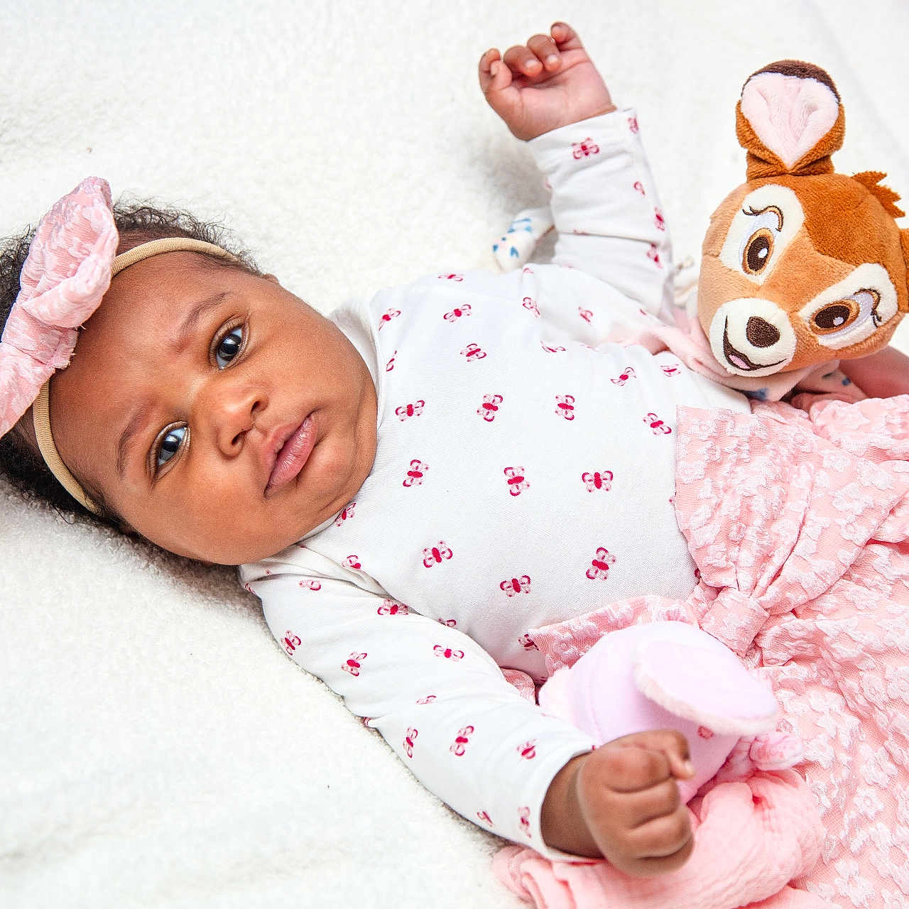 Hope Aÿla a rejoint le concours — aidez-le/la à gagner de superbes lots ! baby, big_eyes, blanket, bow, chubby_cheeks, cozy, curly_hair, floral_pattern, hand, headband, indoor, infant, lying_down, neutral_expression, pink_dress, plush_toy, portrait, skin, soft_texture, stuffed_animal