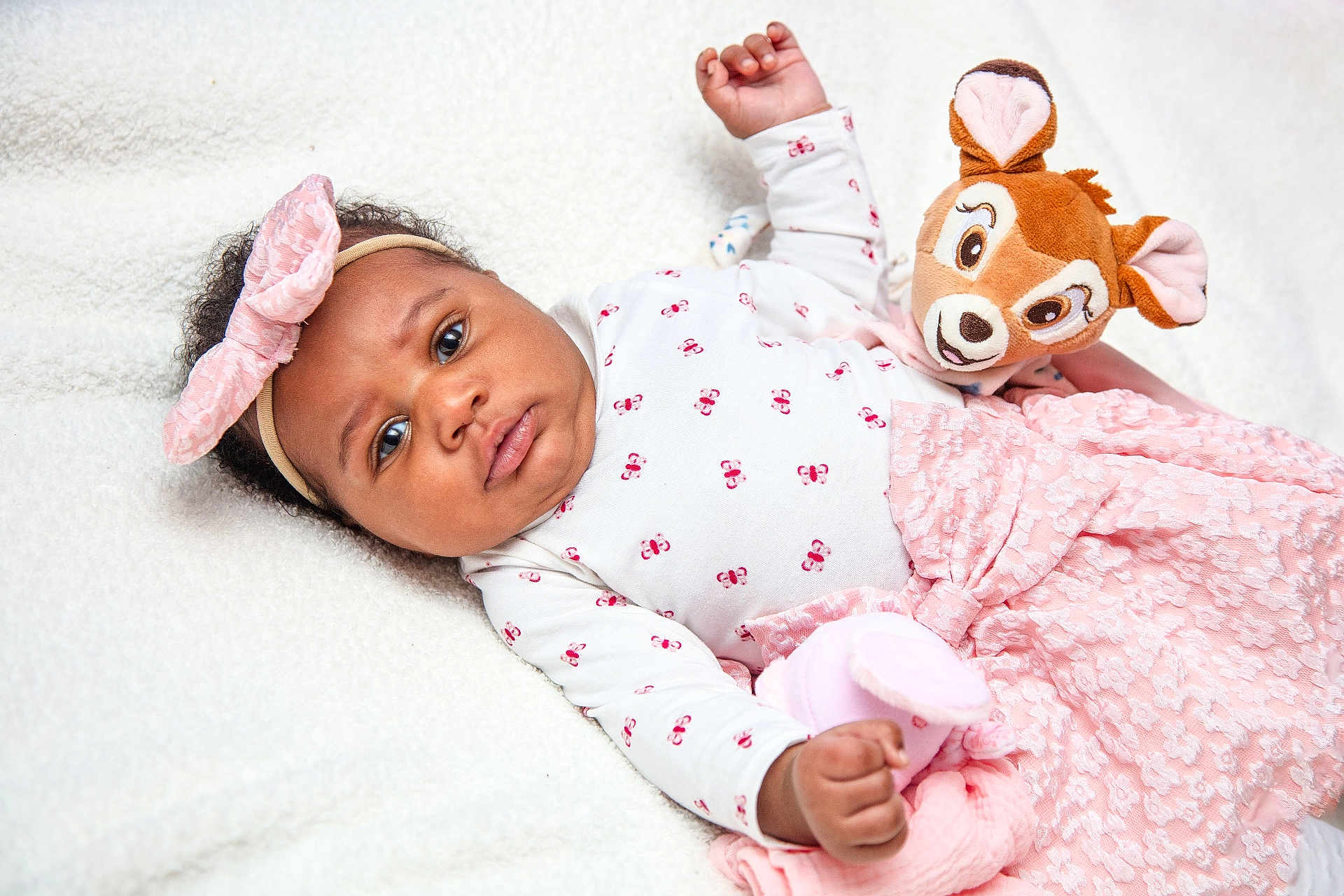 Hope Aÿla a rejoint le concours — aidez-le/la à gagner de superbes lots ! baby, infant, headband, bow, plush_toy, stuffed_animal, blanket, pink_dress, floral_pattern, lying_down, portrait, chubby_cheeks, big_eyes, hand, skin, curly_hair, soft_texture, cozy, indoor, neutral_expression