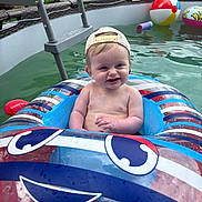 Atlas is registered to the contest to win money with this photo: baby, child, pool, inflatable_float, water, beach_ball, cap, backyard, summer, outdoor, toy, swimming_pool, fun, smiling, sitting, person, recreation, inflatable, cute, happy
