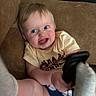 baby, blond_hair, blue_eyes, child, clothing, couch, cute, foot, furniture, happy, holding, indoor, infant, person, playful, relaxed, sitting, smile, sock, toddler