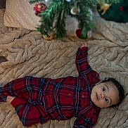 Remi joined the competition — help win amazing prizes! baby, blanket, child, christmas_tree, cozy, cute, decorations, face, festive, green, holiday, indoor, infant, ornaments, pajamas, person, plaid, red, smiling, soft_texture