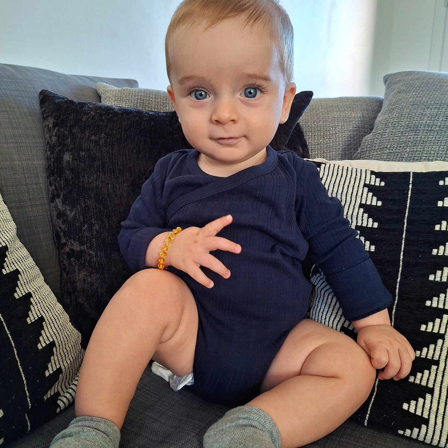 Hyacinthe participe au concours pour gagner de l'argent avec cette photo : baby, blue_eyes, bracelet, child, couch, cozy, cute, expression, furniture, home, indoor, infant, onesie, person, pillow, portrait, sitting, smile, sock, young_child