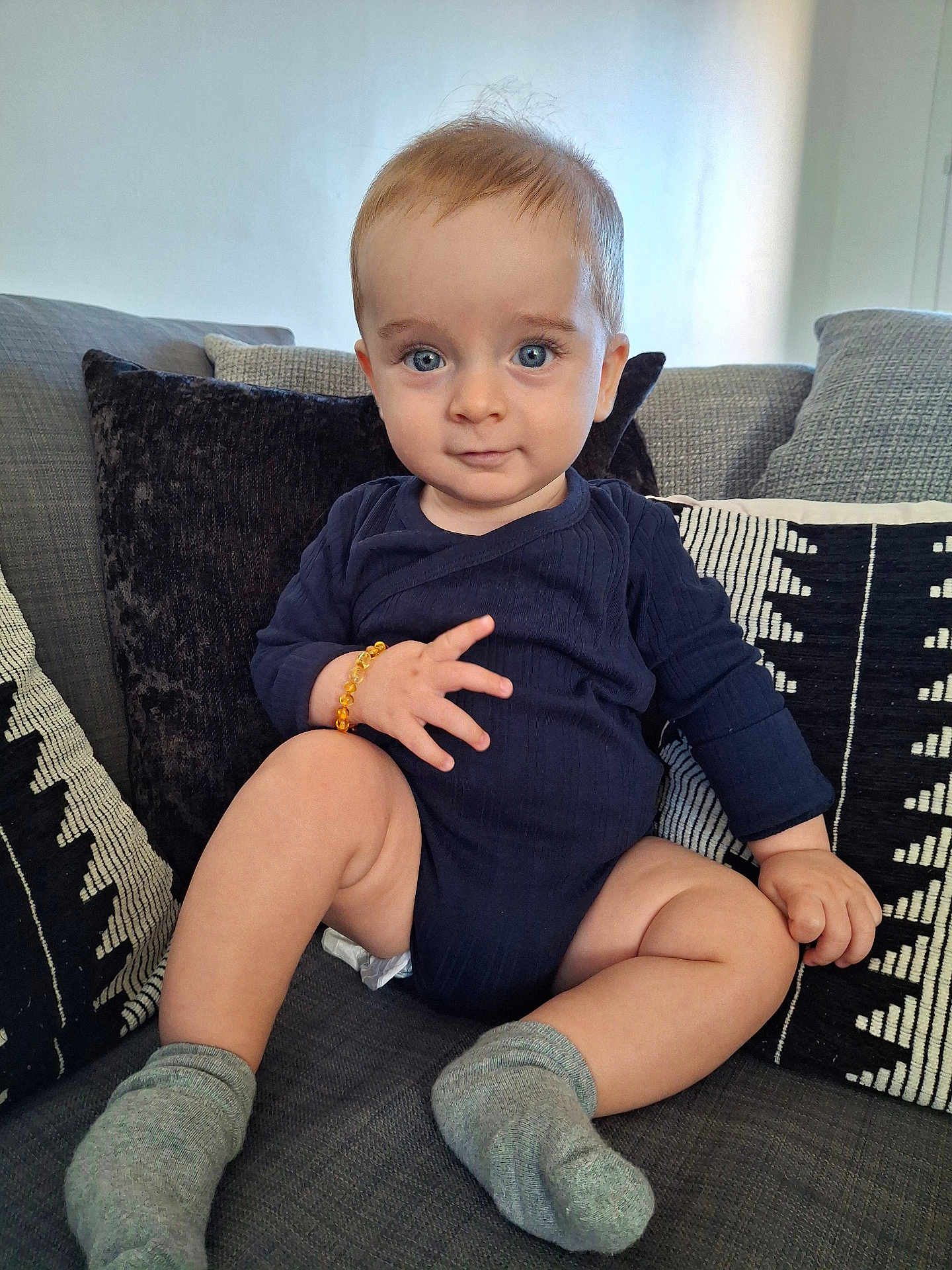 Hyacinthe participe au concours pour gagner de l'argent avec cette photo : baby, blue_eyes, bracelet, child, couch, cozy, cute, expression, furniture, home, indoor, infant, onesie, person, pillow, portrait, sitting, smile, sock, young_child