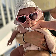 Camëlia participe au concours pour gagner de l'argent avec cette photo : baby, child, sunglasses, hat, white_hat, heart_shaped_glasses, blanket, pink_blanket, arm, hand, person, indoor, blurred_background, cute, fashion, accessory, holding, skin, closeup, portrait