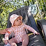 baby, child, outdoor, sun_hat, floral_pattern, chair, hand, trees, fence, daylight, skin, foot, clothing, person, sitting, expression, nature, relaxing, summer, garden