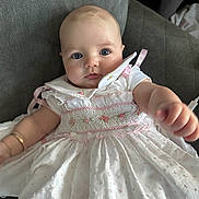 Neiri-Leigh joined the competition — help win amazing prizes! baby, child, dress, white_dress, pink_embroidery, couch, indoor, portrait, cute, infant, young_child, reaching_hand, blue_eyes, face, person, sitting, soft_lighting, furniture, close_up, adorable