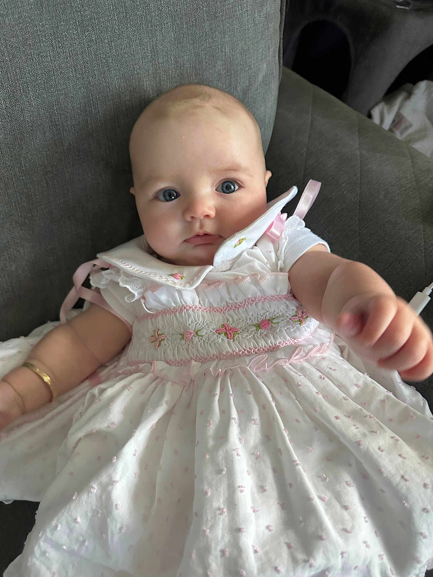 Neiri-Leigh joined the competition — help win amazing prizes! baby, child, dress, white_dress, pink_embroidery, couch, indoor, portrait, cute, infant, young_child, reaching_hand, blue_eyes, face, person, sitting, soft_lighting, furniture, close_up, adorable