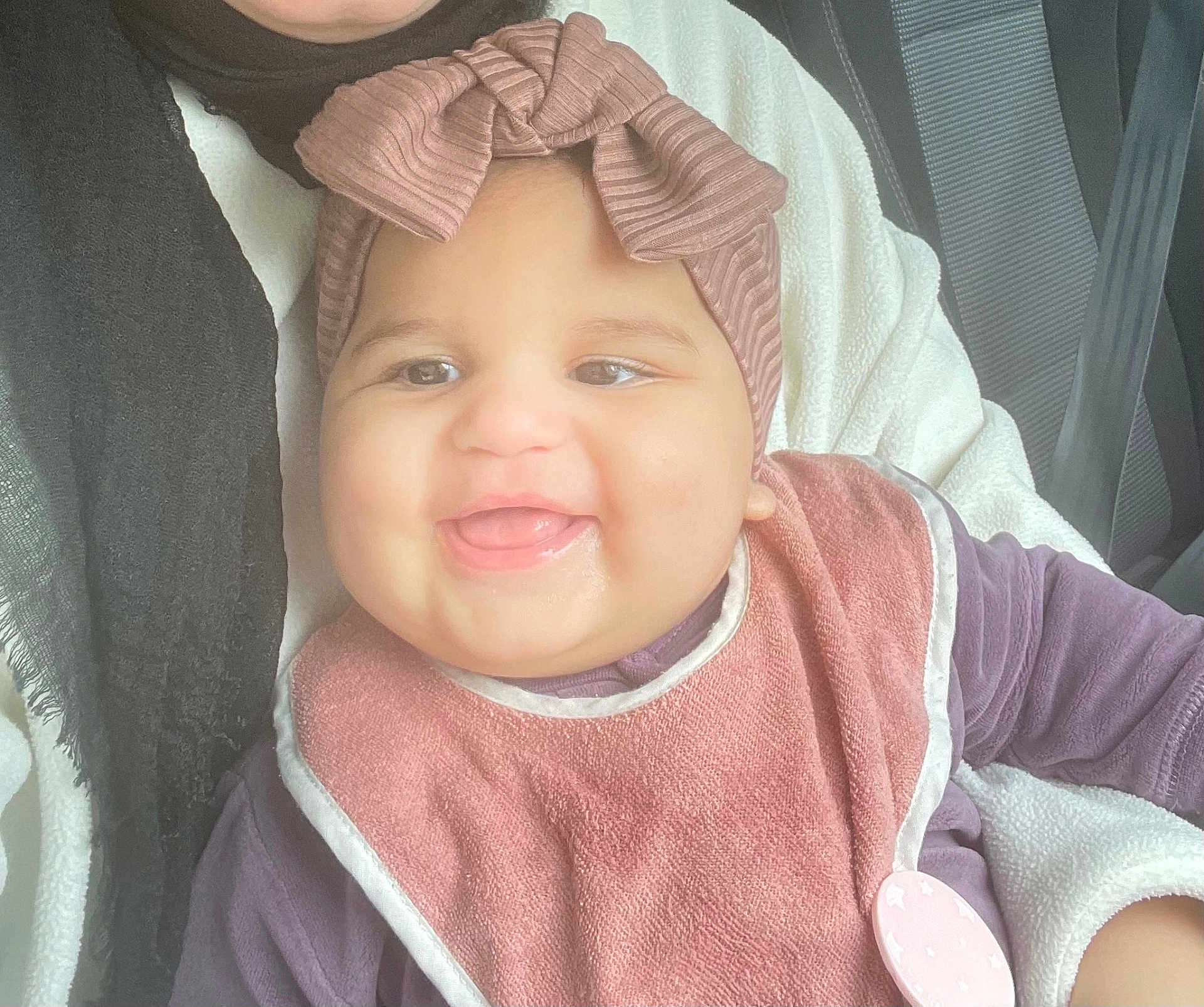 Serine joined the competition — help win amazing prizes! baby, smiling, headband, bow, bib, clothing, person, seatbelt, car_seat, happy, child, portrait, infant, cute, closeup, fabric, pink, purple, hand, holding