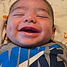 Josiah is registered to the contest to win money with this photo: baby, infant, child, smiling, happy, face, portrait, close_up, eyes_closed, open_mouth, bed, bedding, indoors, clothing, shirt, blue, gray, patterned_background, lying_down, photography