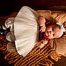 baby, infant, child, dress, headband, blanket, pillow, brown_background, white_dress, red_top, black_shoes, white_socks, portrait, laying_down, cute, indoors, three_months, decor, soft_texture, cozy
