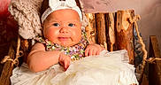 Delanis is registered to the contest to win money with this photo: baby, child, infant, headband, bow, sequin_clothing, tutu, white_tutu, knitted_blanket, wooden_chair, floral_background, cute, portrait, smiling, indoors, cozy, plush, sitting, happy, person