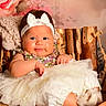 baby, child, infant, headband, bow, sequin_clothing, tutu, white_tutu, knitted_blanket, wooden_chair, floral_background, cute, portrait, smiling, indoors, cozy, plush, sitting, happy, person