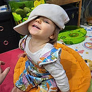 Lilith participe au concours pour gagner de l'argent avec cette photo : toddler, child, smiling, hat, colorful_clothing, sitting, orange_cushion, indoor, toys, play_area, happy, person, cute, face, long_sleeve, patterned_outfit, hand, furniture, young, playful