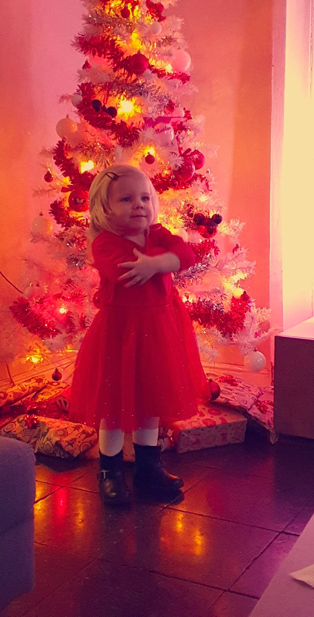 Noélya a rejoint le concours — aidez-le/la à gagner de superbes lots ! baby_toddler_clothing, child, christmas, christmas_decoration, christmas_eve, christmas_tree, dress, floor, flooring, holiday, home, human_body, interior_design, ornament, peach, person, pink, red, room, toddler