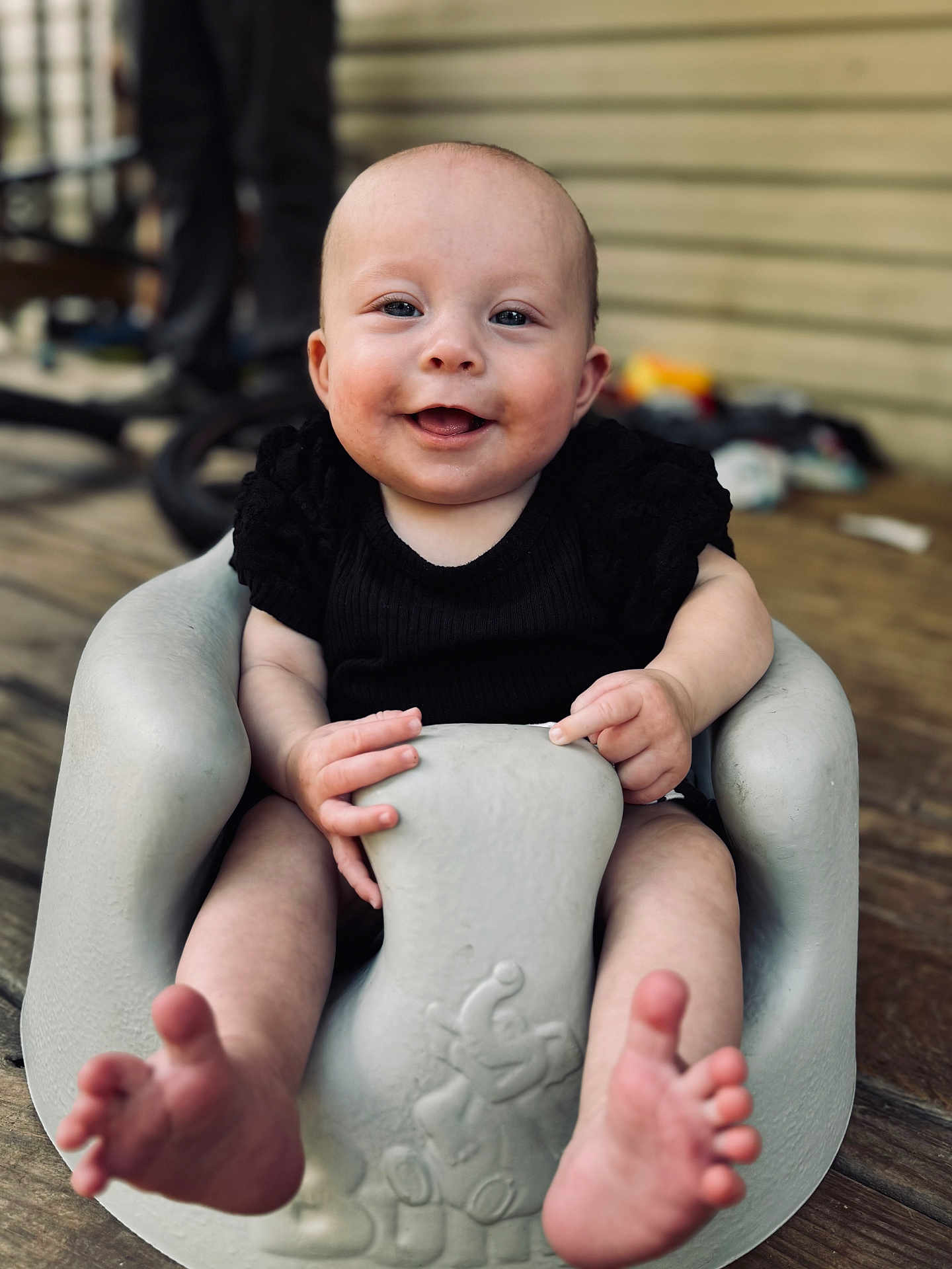 Baylor joined the competition — help win amazing prizes! baby, smiling, infant, seat, foot, hand, wood_floor, porch, black_clothing, face, happy, child, indoors, skin, small_toes, molded_seat, expression, person, cute, sitting