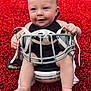 Baylor is registered to the contest to win money with this photo: baby, infant, football_helmet, red_background, barefoot, smiling, cute, sport, outdoor, child, helmet_straps, sitting, skin, legs, hands, face, head, happy, playful, closeup