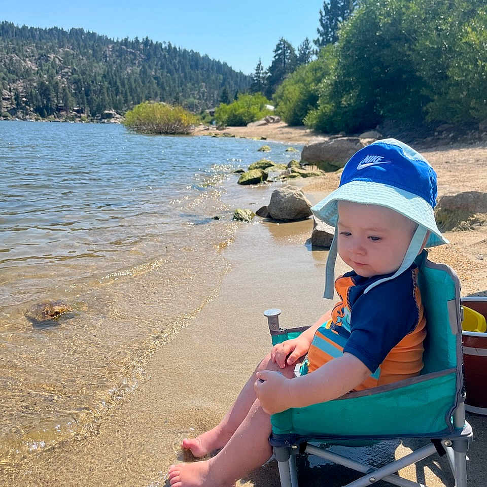 Caydence is registered to the contest to win money with this photo: beach_chair, blue_sky, child, footwear, forest, hat, lake, nature, outdoor, reflection, relaxation, rocks, sand, summer, sunlight, swimsuit, toddler, trees, vacation, water