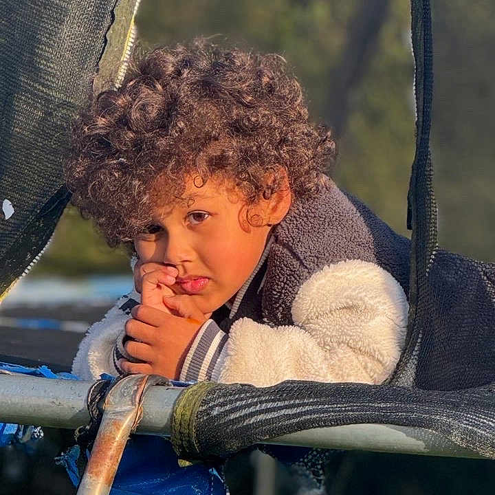 Kinsey a rejoint le concours — aidez-le/la à gagner de superbes lots ! blue_tarp, casual, child, curly_hair, daylight, expression, forest, jacket, leisure, metal_frame, nature, netting, outdoor, person, playground, portrait, texture, thoughtful, trampoline, young