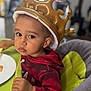 background_blur, brown_eyes, casual_clothing, child, crown, curious, earring, expression, face, food, high_chair, indoor, inflatable, person, plate, red_hoodie, seat, table, toddler, young_child