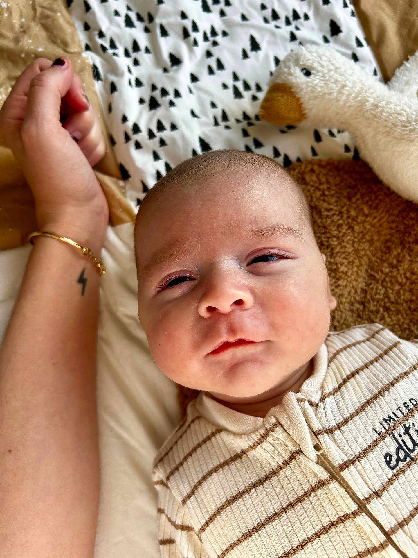 Antonin a rejoint le concours — aidez-le/la à gagner de superbes lots ! baby, infant, face, onesie, striped_clothing, plush_toy, duck, tattoo, arm, bracelet, sleepy, closeup, bed, blanket, soft_toy, person, skin, expression, indoors, child