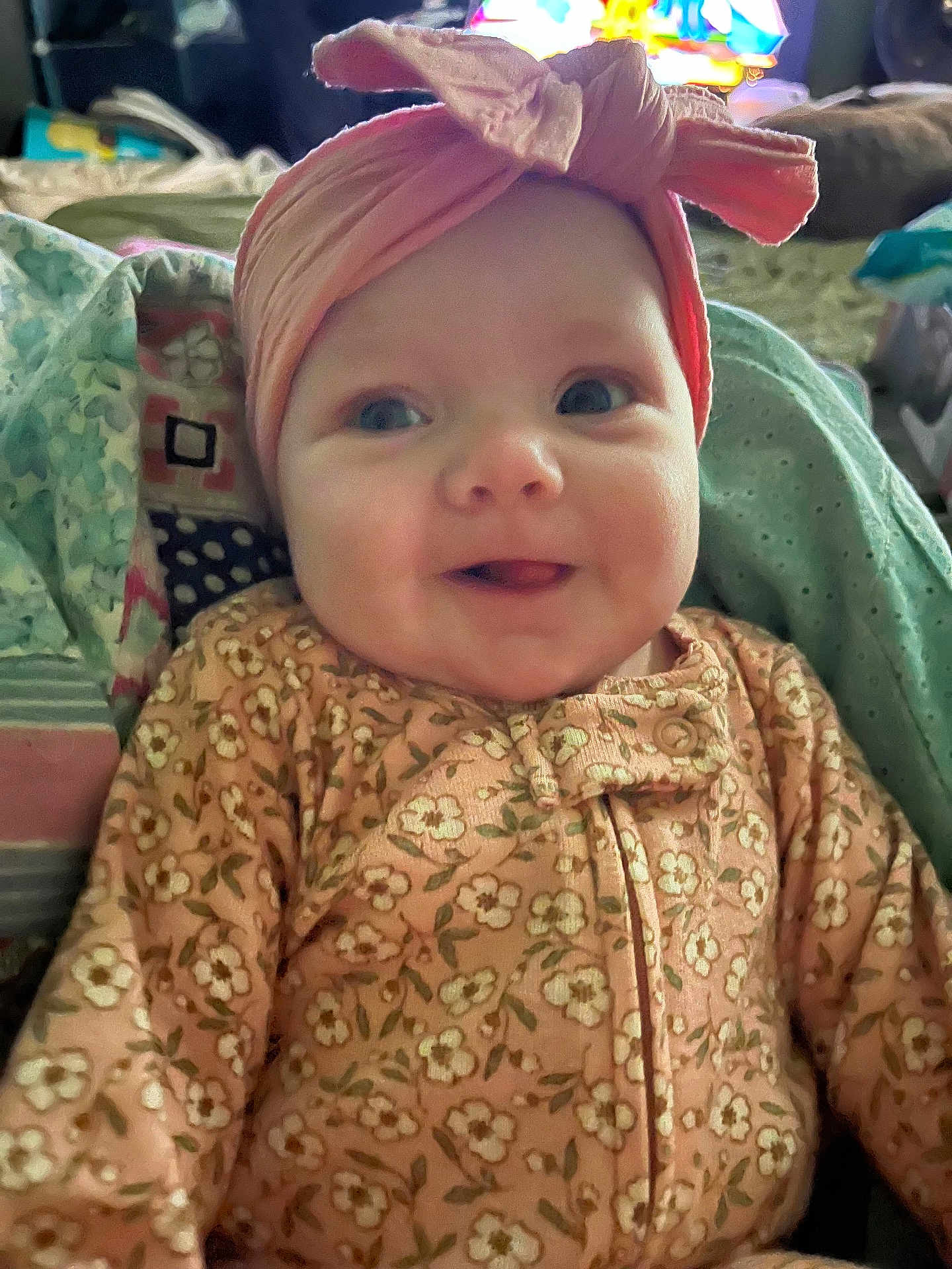 Drew is registered to the contest to win money with this photo: baby, infant, headband, bow, smile, tongue, onesie, floral_pattern, blanket, cozy, cute, child, portrait, happy, indoors, soft_lighting, face, clothing, expression, comfort