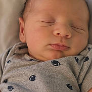 Robert is registered to the contest to win money with this photo: newborn, baby, sleeping, infant, onesie, football_pattern, blanket, closeup, peaceful, cute, soft_lighting, portrait, child, resting, indoors, human, face, head, skin, comfort