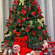 Sebastien a rejoint le concours — aidez-le/la à gagner de superbes lots ! child, christmas_tree, santa_claus_costume, red_bow, christmas_decorations, ornaments, holiday, festive, smiling, thumbs_up, pillow, indoors, christmas_lights, red_mat, holiday_spirit, happy_child, celebration, christmas_toys, santa_doll, festive_scene