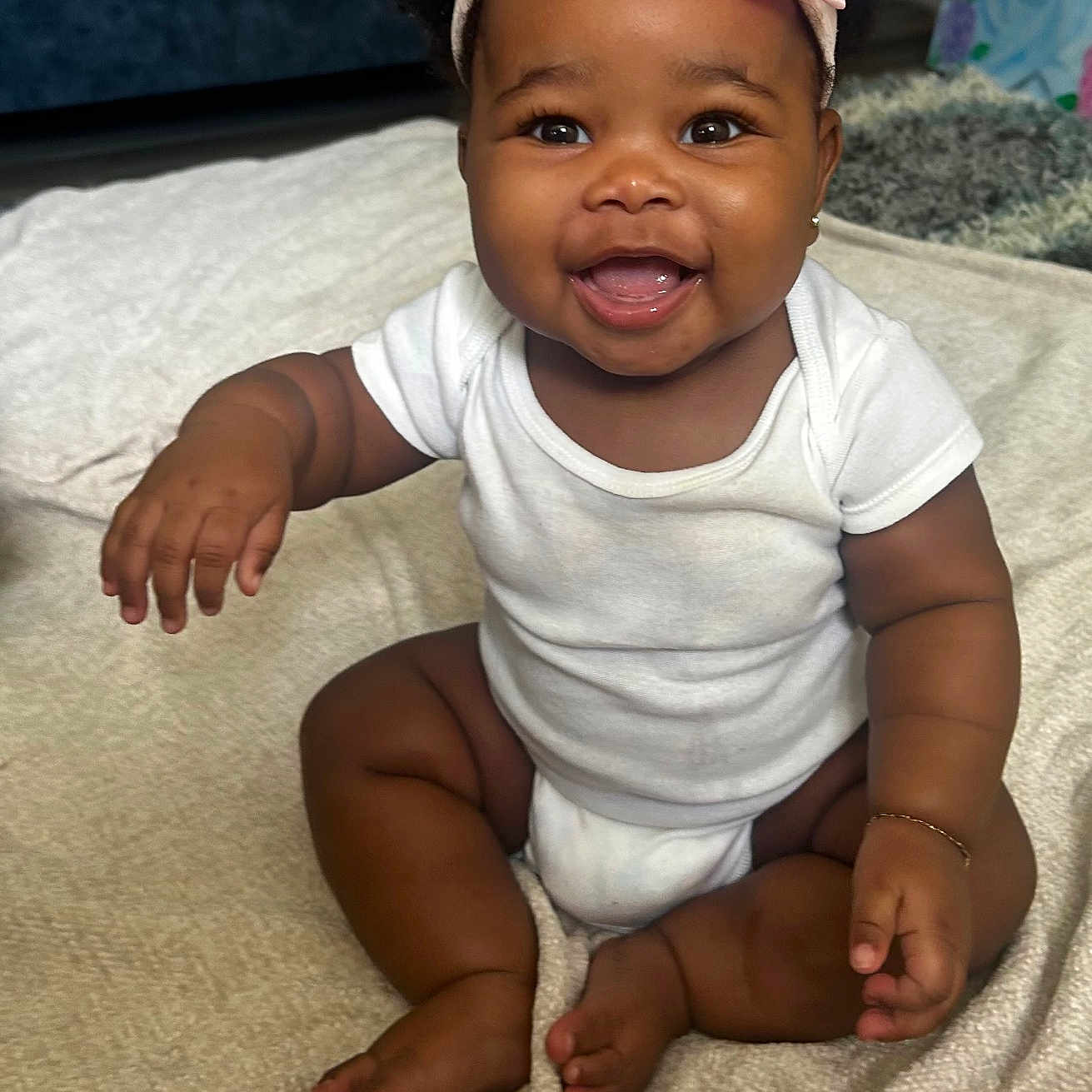Kori is registered to the contest to win money with this photo: baby, smiling, headband, pink_bow, white_onesie, sitting, blanket, indoor, happy, child, cute, portrait, infant, furniture, cozy, living_room, skin, face, expression, cute_baby