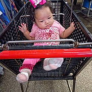 Musica is registered to the contest to win money with this photo: baby, shopping_cart, pink_bow, pink_clothing, socks, curly_hair, indoor, floor, clothing_racks, metal, shopping, child, person, retail, store, cart_handle, expression, footwear, seat, shopping_area
