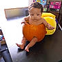 arms, autumn, baby, black_table, child, curly_hair, cute, expression, face, festive, hollow_pumpkin, indoor, legs, orange, plush_toy, pumpkin, puzzle_boxes, sitting, table, toy