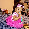 baby, bedspread, child, clothing, cute, face, foot, furniture, hair, hand, headband, indoor, pattern, person, pink_tutu, playful, room, sitting, toddler, toy