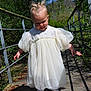 baby, bridge, child, cute, daytime, dress, exploring, greenery, hair_ties, nature, outdoor, park, person, sandals, shadow, sunlight, toddler, white_dress, wooden_bridge, young_child