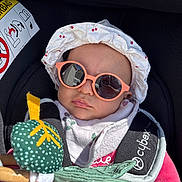 Lya a rejoint le concours — aidez-le/la à gagner de superbes lots ! baby, sunglasses, hat, car_seat, toy, reflection, sunlight, clothing, pink, white, green, child, infant, safety_strap, cute, outdoor, accessory, face, person, headwear