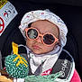 baby, sunglasses, hat, car_seat, toy, reflection, sunlight, clothing, pink, white, green, child, infant, safety_strap, cute, outdoor, accessory, face, person, headwear